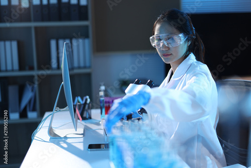 Фотография Woman scientist in safety glasses and lab coat conducting a biomedical experiment using a microscope and test tubes in a research lab