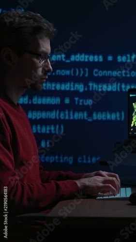Side view, coder at a dark office desk works late at night, with programming script on a background. Data scientist working on a machine learning or artificial intelligence task. Vertical video