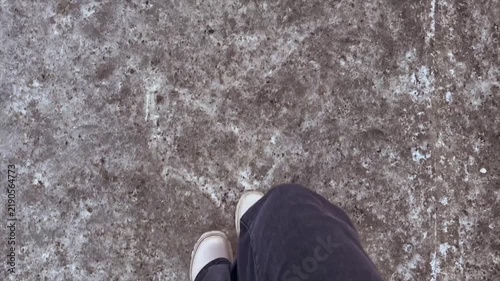 First person view of legs in light boots and dark trousers walking on frozen asphalt and snow