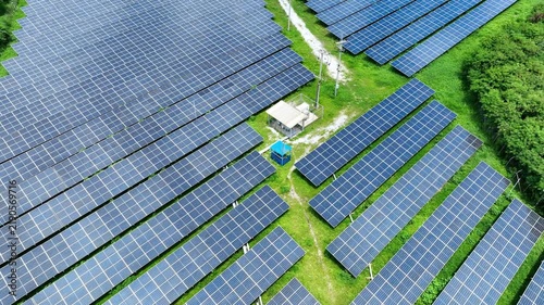 Rows of photovoltaic panels stretch across green land in this aerial view, representing clean energy production, environmental responsibility and the growing transition toward a net zero future. 4k.
