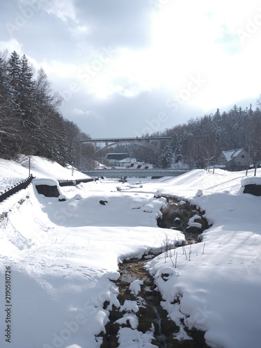 Fotografie Snow-covered river valley with stream conifers and bridge Hokkaido