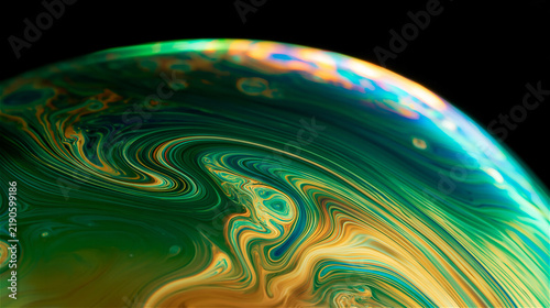 Abstract photo of soap bubble film surface, thin iridescent membrane with swirling color patterns, deep emerald and gold tones. AI gen
