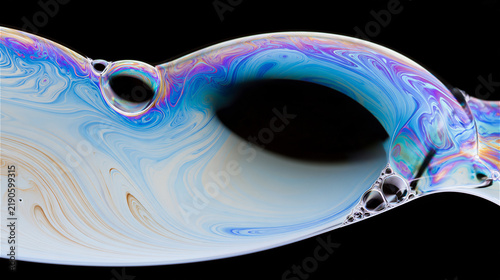 Abstract photo of soap bubble film surface, thin iridescent membrane with swirling color patterns, icy silver and pale blue tones. AI gen