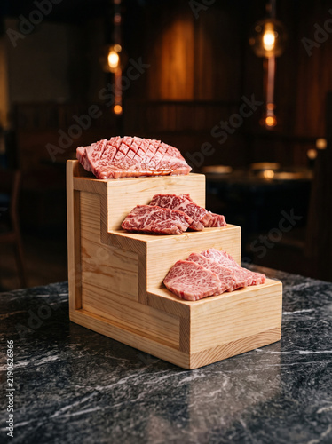 Raw premium marbled wagyu beef cuts displayed on wooden staircase stand on dark marble restaurant table
