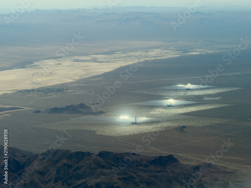 Aerial view of solar thermal plants with bright glowing towers, mirror arrays, and a dry lakebed beyond, Mojave Desert, California