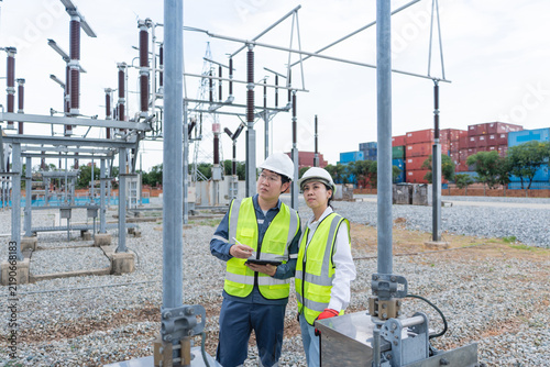 Quadro su tela Two substation engineers conduct a substation inspection patrol, examining a disconnect switch with a tablet beneath a lattice transmission tower
