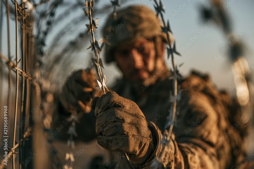 Obraz premium Soldier's hand gripping barbed wire fence, depicting military conflict and defense