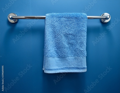 a single light blue bath towel hangs neatly on a modern metallic towel rack affixed to a textured blue wall