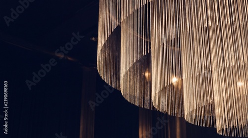 Modern metallic fringe chandelier with warm spotlight illumination against dark interior background
