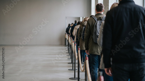 People waiting in line indoors with ropes