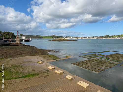 Obraz na plátne Low tide reveals a textured slipway and tidal shoreline along Strangford Lough, with Portaferry visible across the water beneath dramatic white clouds and blue sky