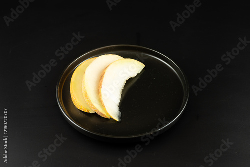 Sliced ripe melon served on a single black plate against a dark black background. Dark food photography, fresh sweet summer fruit.