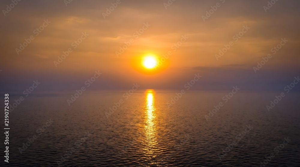 Fototapeta premium Golden sun setting over a calm ocean with a bright reflection on the shimmering water surface
