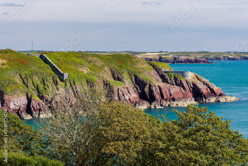 Fotografie Historic coastal defence walls built into rocky headland, lush gorse and bracken