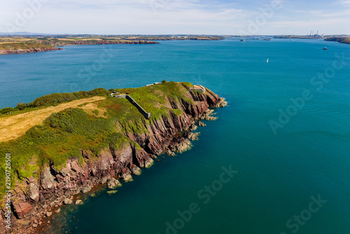 Bild auf Leinwand Rugged red sea cliffs topped with green gorse and stone fortifications, clear co