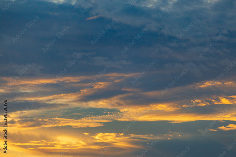Obraz premium Dramatic sunset sky with golden and dark blue clouds creating a beautiful natural spectacle