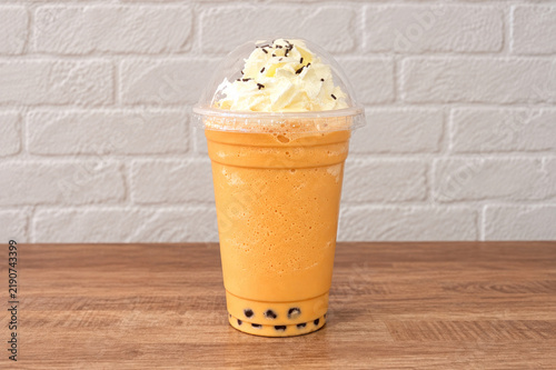 A high-quality photo mock-up of Thai bubble tea in a clear plastic cup with a domed lid, filled with creamy iced tea with black tapioca pearls, on a kitchen counter