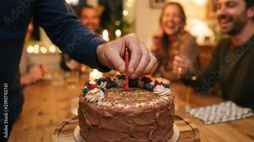 Hand placing red candle on birthday cake at dinner party