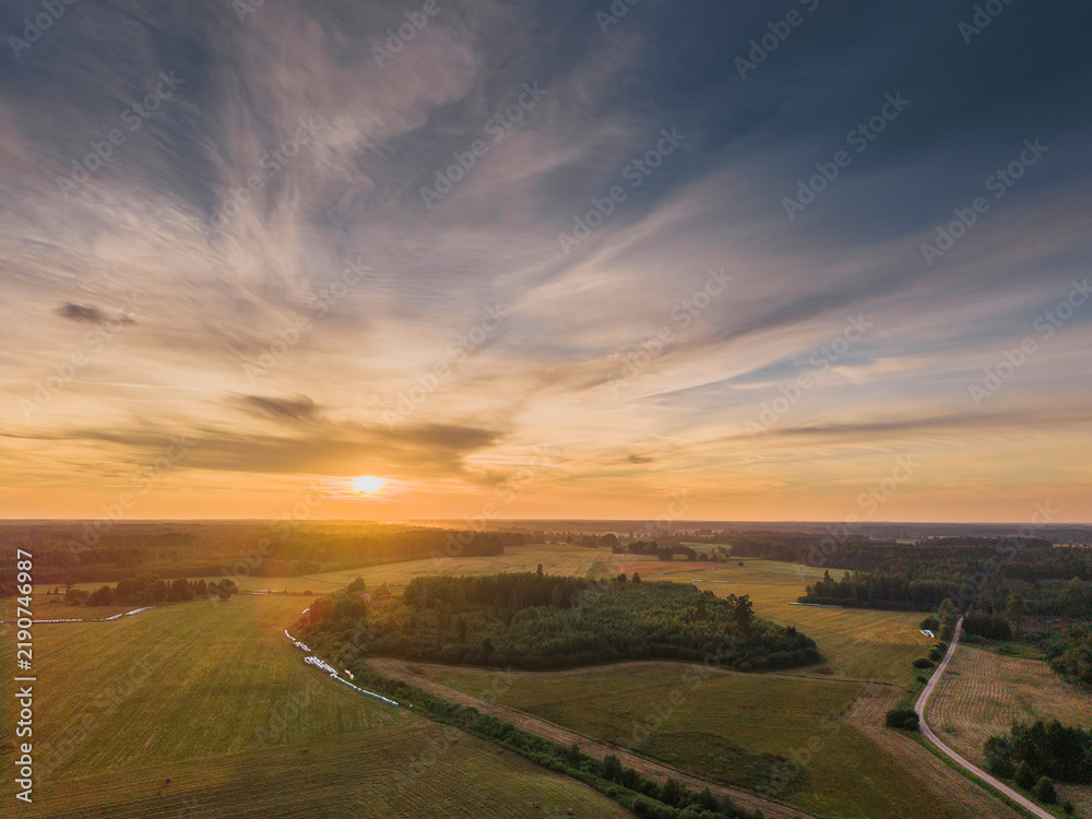 Obraz premium Sunset paints golden sky over rolling green fields and winding paths. Warm light bathes landscape in peaceful, serene glow. Ideal for nature, travel, or countryside-themed projects