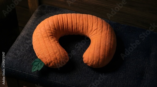 Orange pumpkin shaped travel neck pillow resting on dark cushioned chair for autumn holiday trip and ergonomic comfort mockup