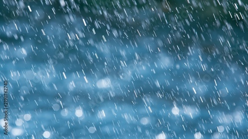 Heavy rain falling against a blurred blue background, creating dynamic diagonal streaks and atmospheric bokeh