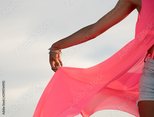 African Woman hand holding neon pink fabric of a dress against a bright sky. Copy space fashion concept