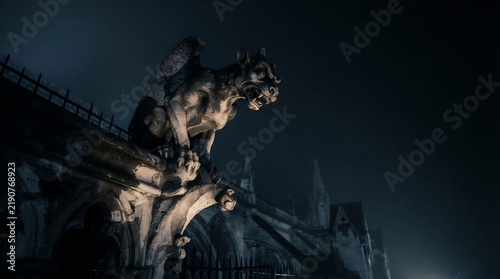 Gothic gargoyle statue perched on cathedral roof at foggy night, spooky Halloween atmosphere, dark stone demon sculpture, eerie cinematic gothic architecture