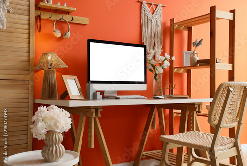 Interior of office with workplace, artificial flowers in vases and shelf unit