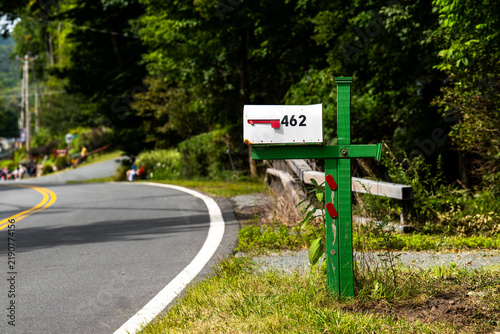 White mailbox numbered 462 marks a driveway along a winding country road, surrounded by summer greenery, illustrating rural living, property access and small town America.