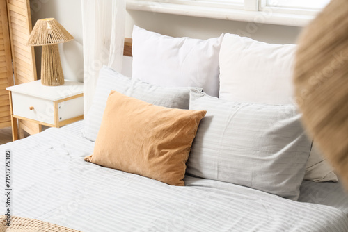 Cozy bed with grey bed sheets and colorful pillows in stylish bedroom