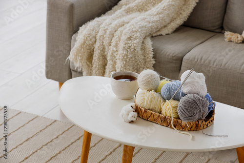 Basket with knitting yarn, cotton flowers and cup of coffee on table in livin...