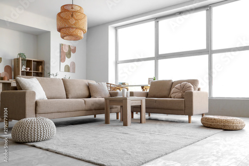 Interior of stylish living room with cozy grey sofas, coffee table and pouf n...
