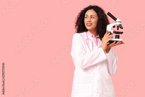 Female African-American doctor with microscope on pink background