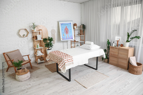 Interior of massage therapists office with couch, shelving units and poster o...