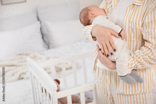 Mother holding cute little sleeping baby with pacifier in bedroom at home, cl...
