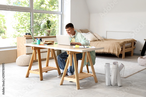Teenage boy studying with laptop at table in bedroom