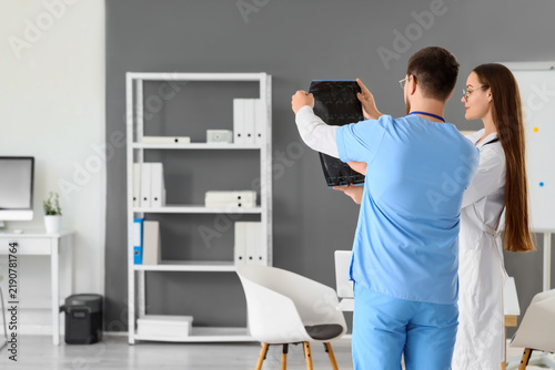 Young doctors studying x-ray image of spine in clinic, back view
