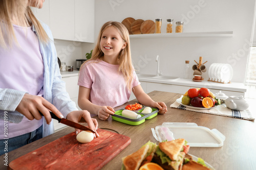 Happy mother with daughter cooking food for school lunchbox in kitchen