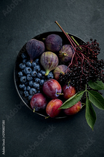Fresh organic purple fruits and berries on a dark ceramic plate