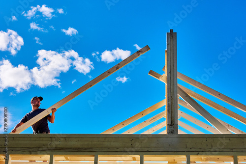 Konstfotografi Setting rafter onto ridge beam and wall plate, young builder positions roof member for timber frame assembly