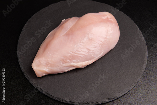Fotografie Raw chicken breast background closeup with single fresh poultry fillet chunk on black slate plate, organic meat protein ingredient top view flat lay over dark surface, horizontal minimal copy space
