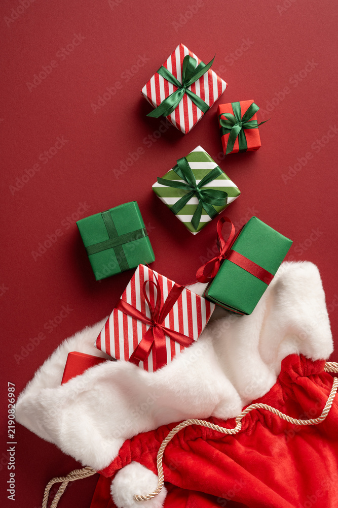 Naklejka premium Merry Christmas and Happy New Year with Santa Claus presents in festive red and green wrapping on vertical maroon background