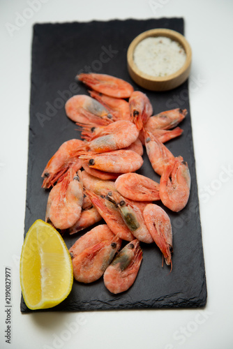 Konstfotografi The black stone plaque has an overhead view of a handful of frozen shrimp, complemented by a small wooden container with salt and a bright slice of lemon