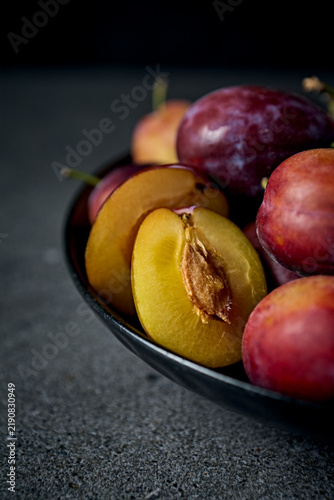 Fresh organic plums with yellow slice in a ceramic bowl