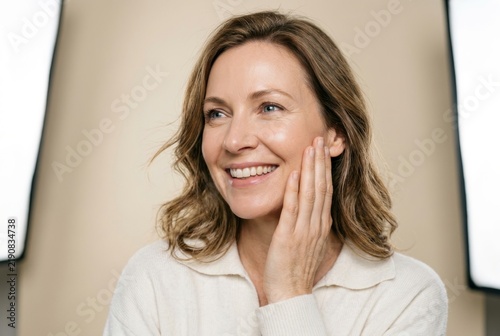 An overjoyed mature lady with ideal appearance touches her cheek after salon spa procedures.