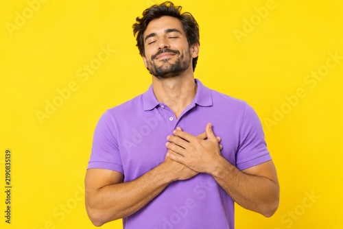 Attractive kind man in lilac shirt touching his heart with closed eyes.