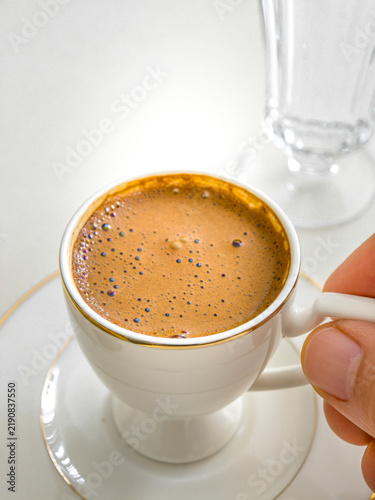 Hand Holding Handle of White Porcelain Cup Filled with Foamy Turkish Coffee