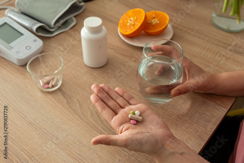 Female hand displaying mixed pills and capsule while holding water near fresh orange at home. Concept of polypharmacy, nutritional supplements, immunity care and medication management.