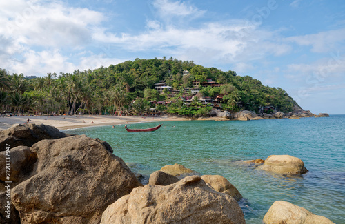 Granite rocks and wooden boat in tropical bay with lush green hill