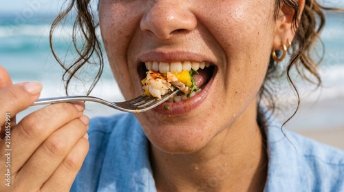 Close up of a woman eating a shrimp and mango salad with a fork at the beach